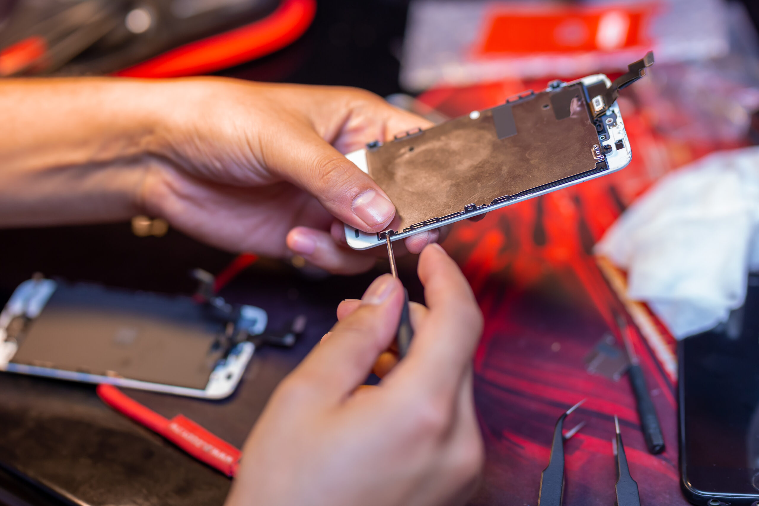 A man is repairing a mobile phone. In the frame, his hands and details of the device. repair shop for gadgets